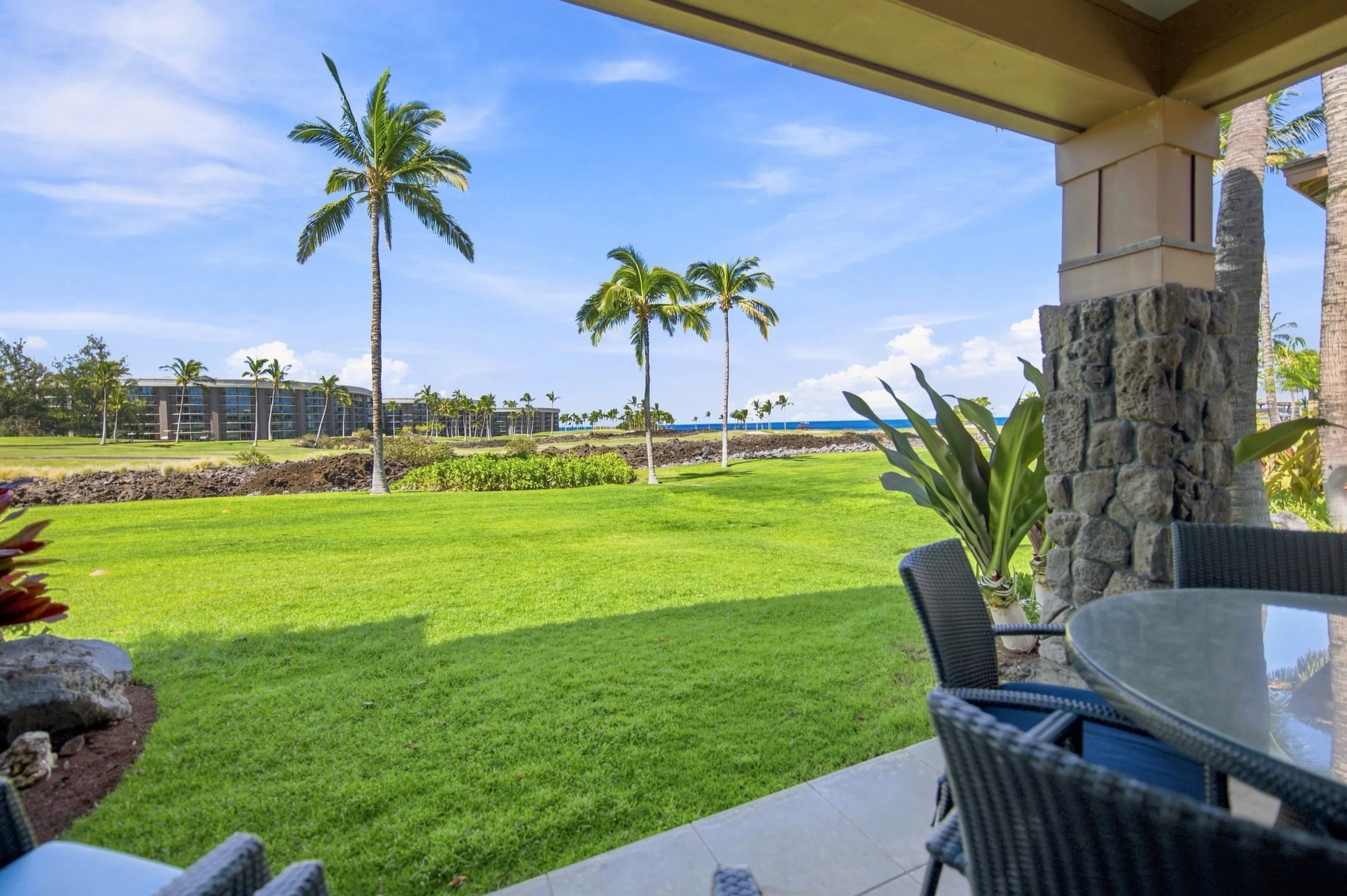 View from the covered lanai across the lawn and golf course to the ocean, with palms and a lava rock pillar