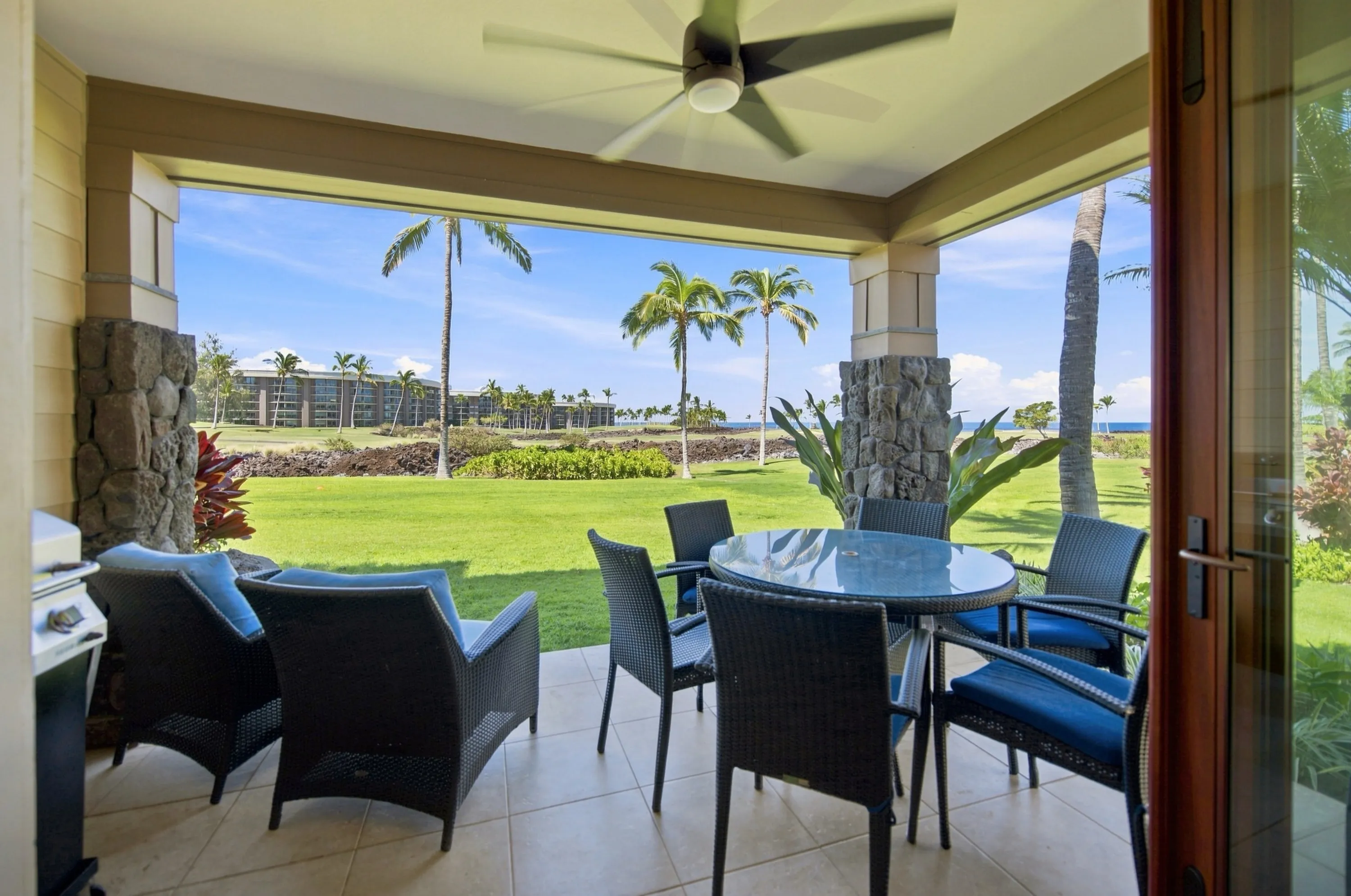 Covered lanai with lounge seating and a dining table, looking across the golf course to the ocean