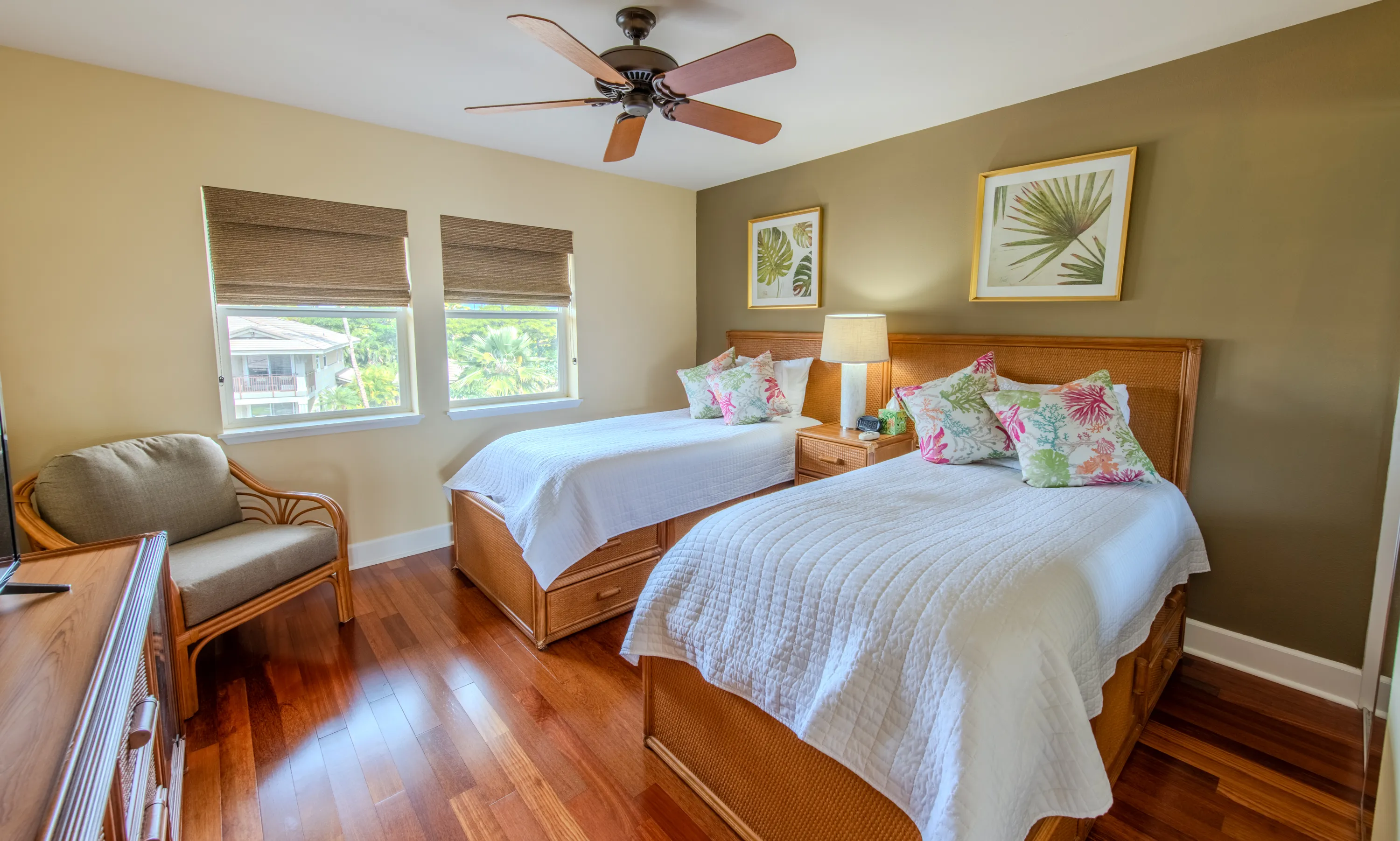 Bedroom with two twin beds, woven rattan frames, and palm-print art