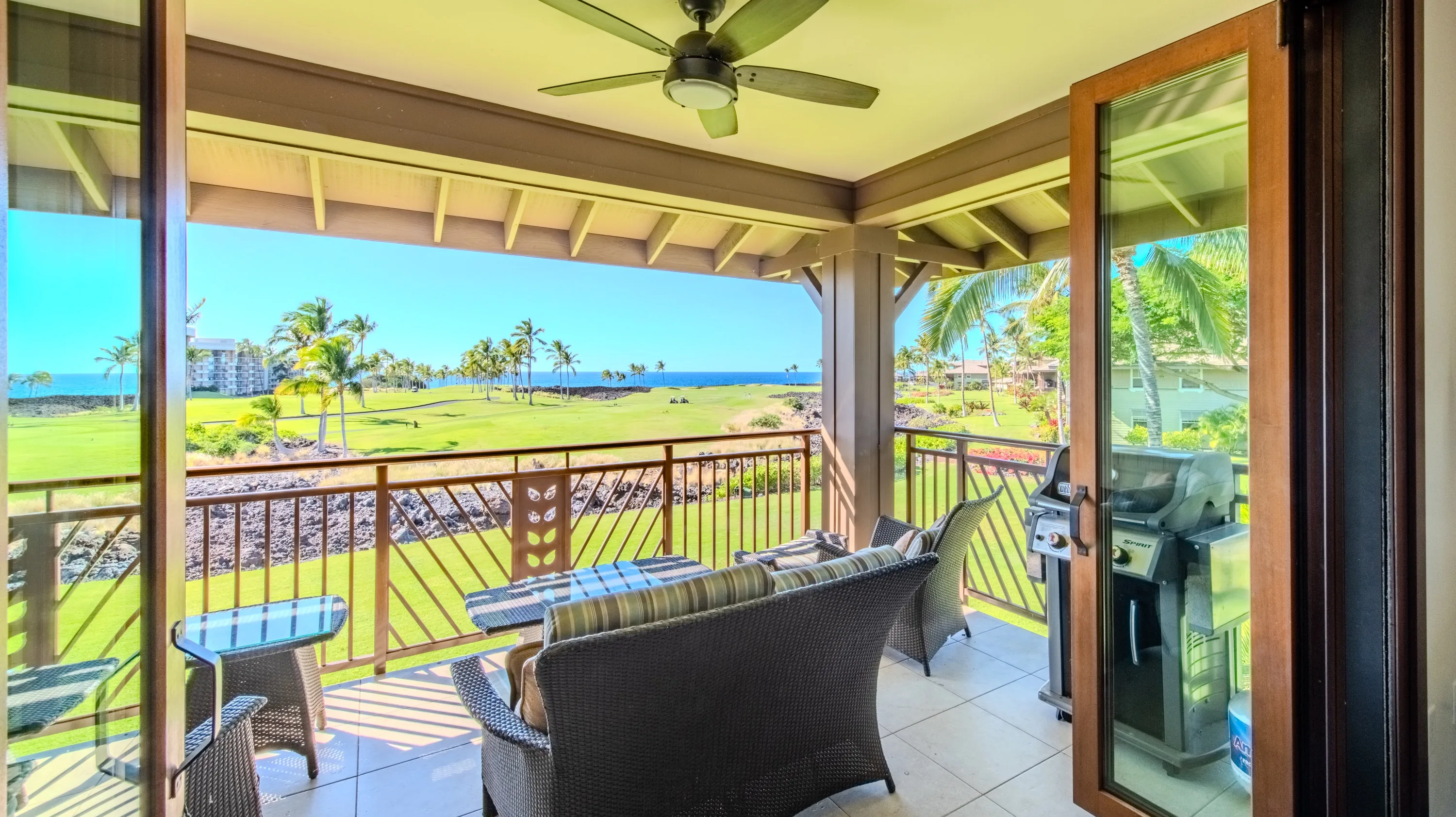 Covered lanai at the Hale Maluhia Suite with wicker seating and a gas grill, looking across the golf fairway to the Pacific