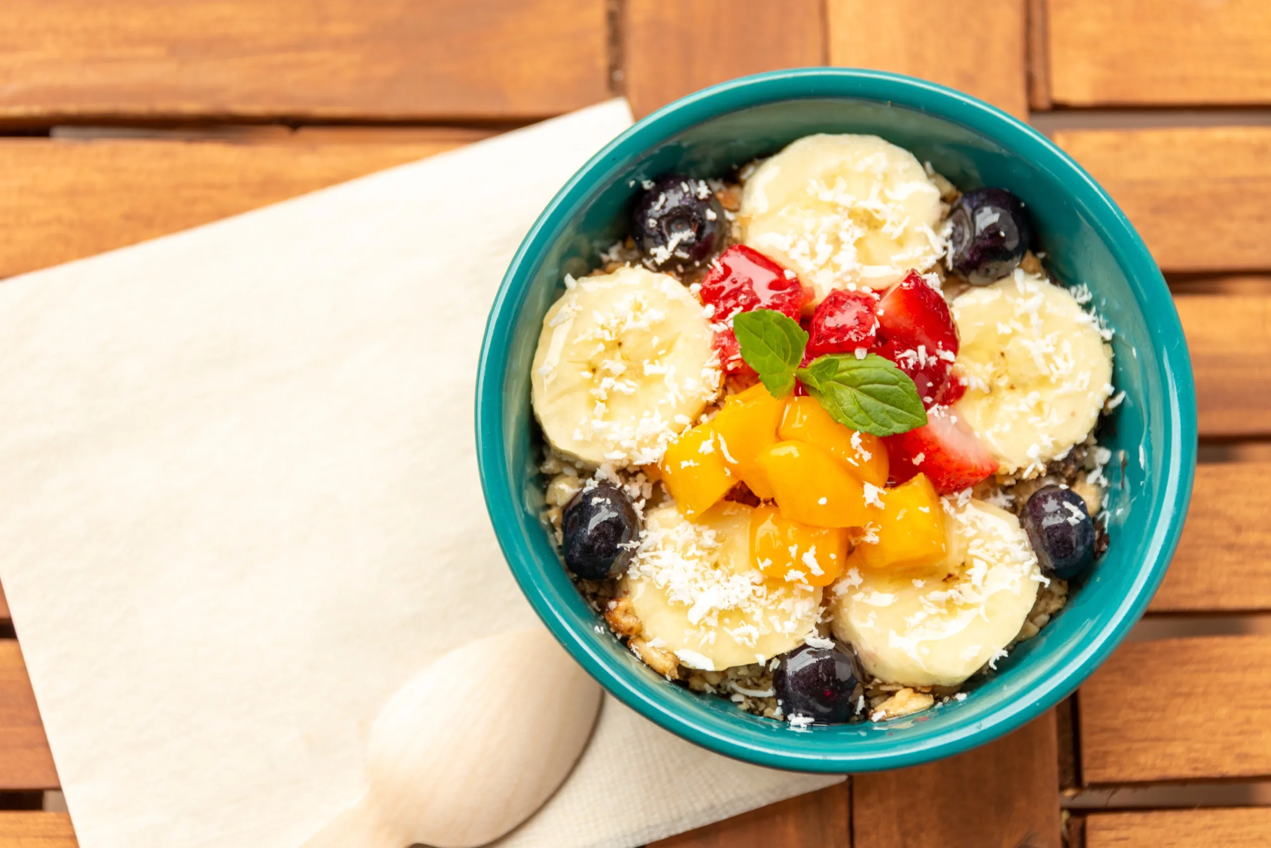 A fresh fruit and granola breakfast bowl with banana, berries, mango, and coconut