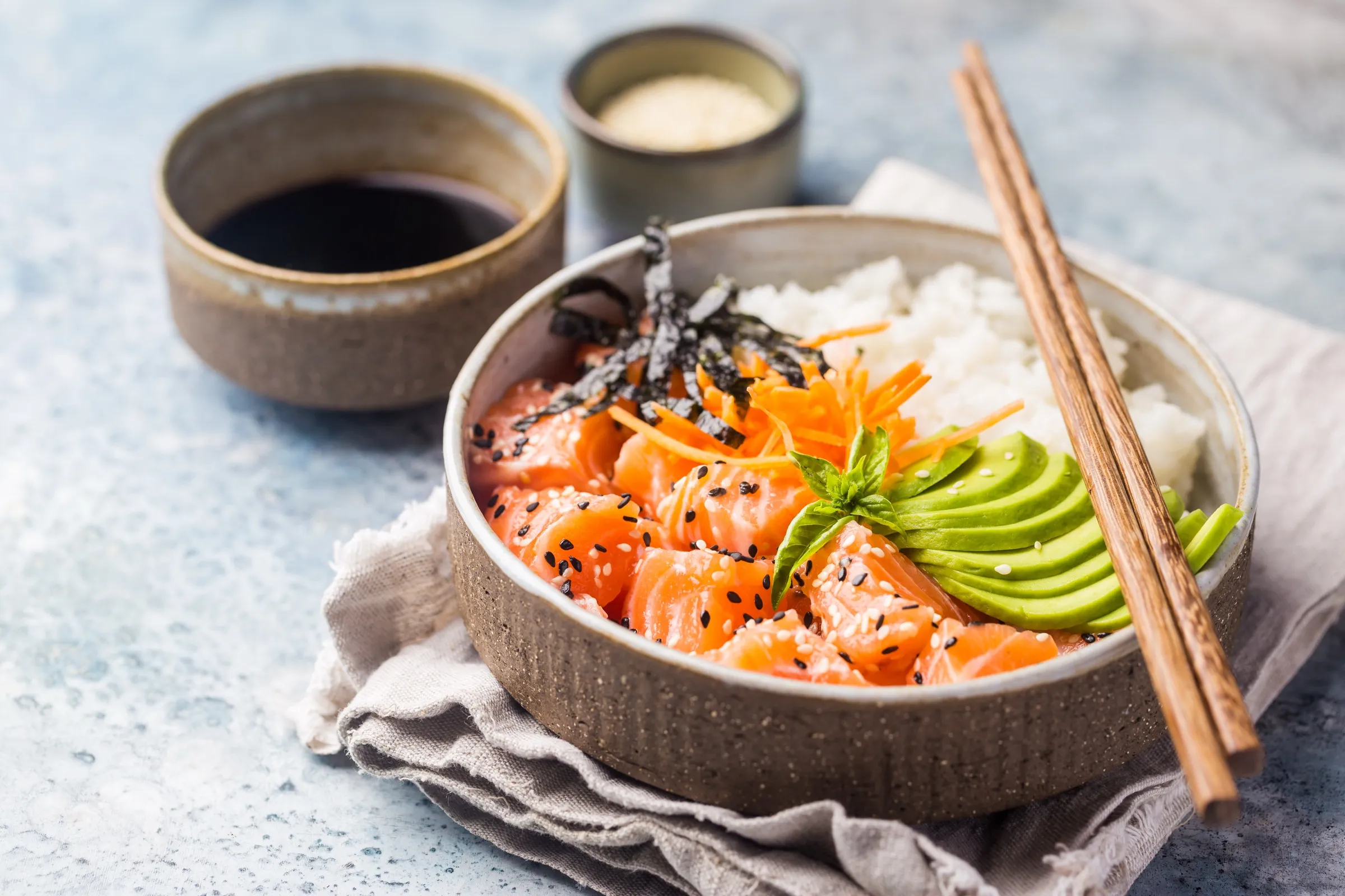 A fresh salmon poke bowl with rice, avocado, and chopsticks