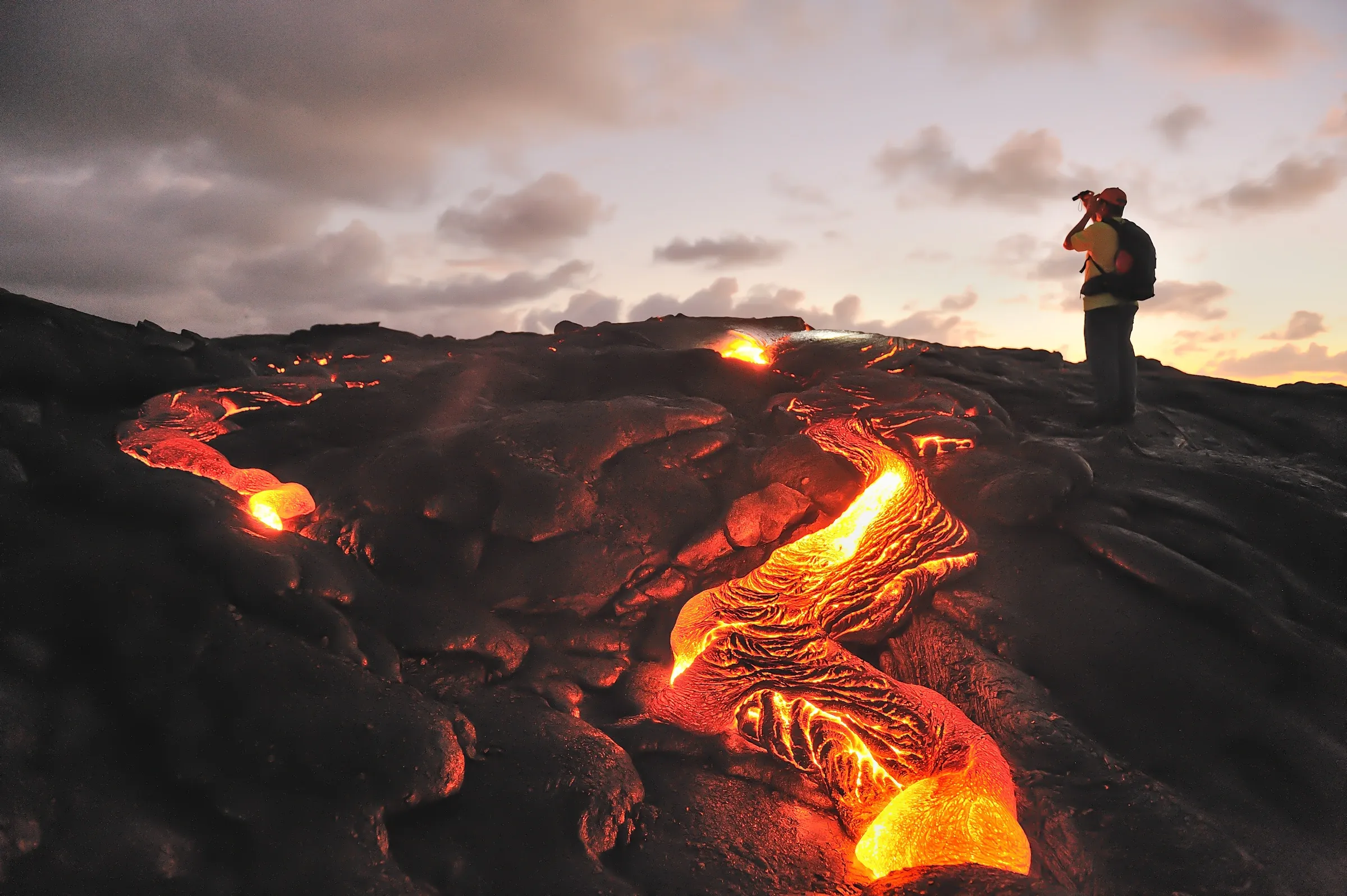 Molten lava glowing across black rock on Kīlauea at dusk