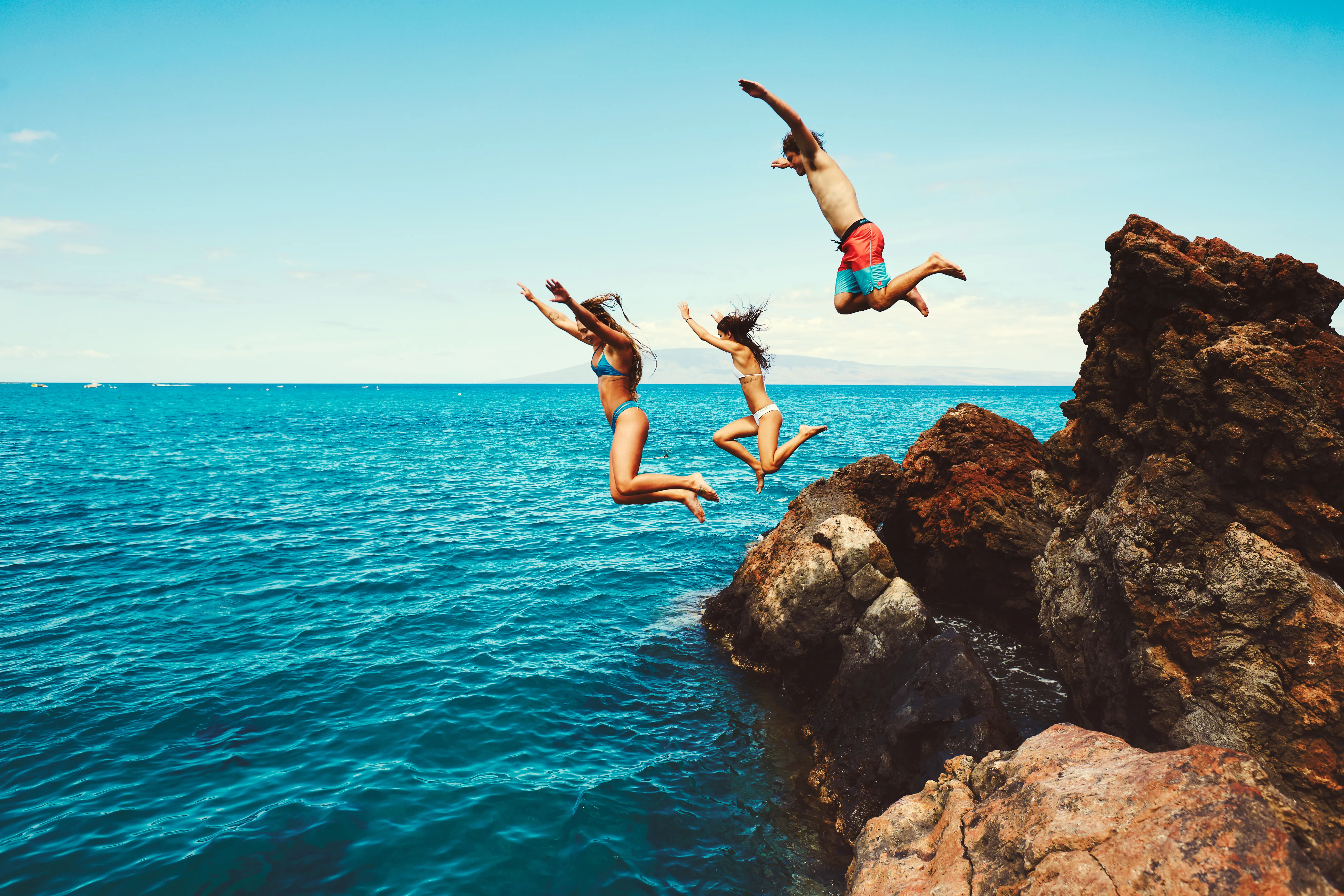 Two people leaping from lava rock into the turquoise ocean on the Kohala Coast