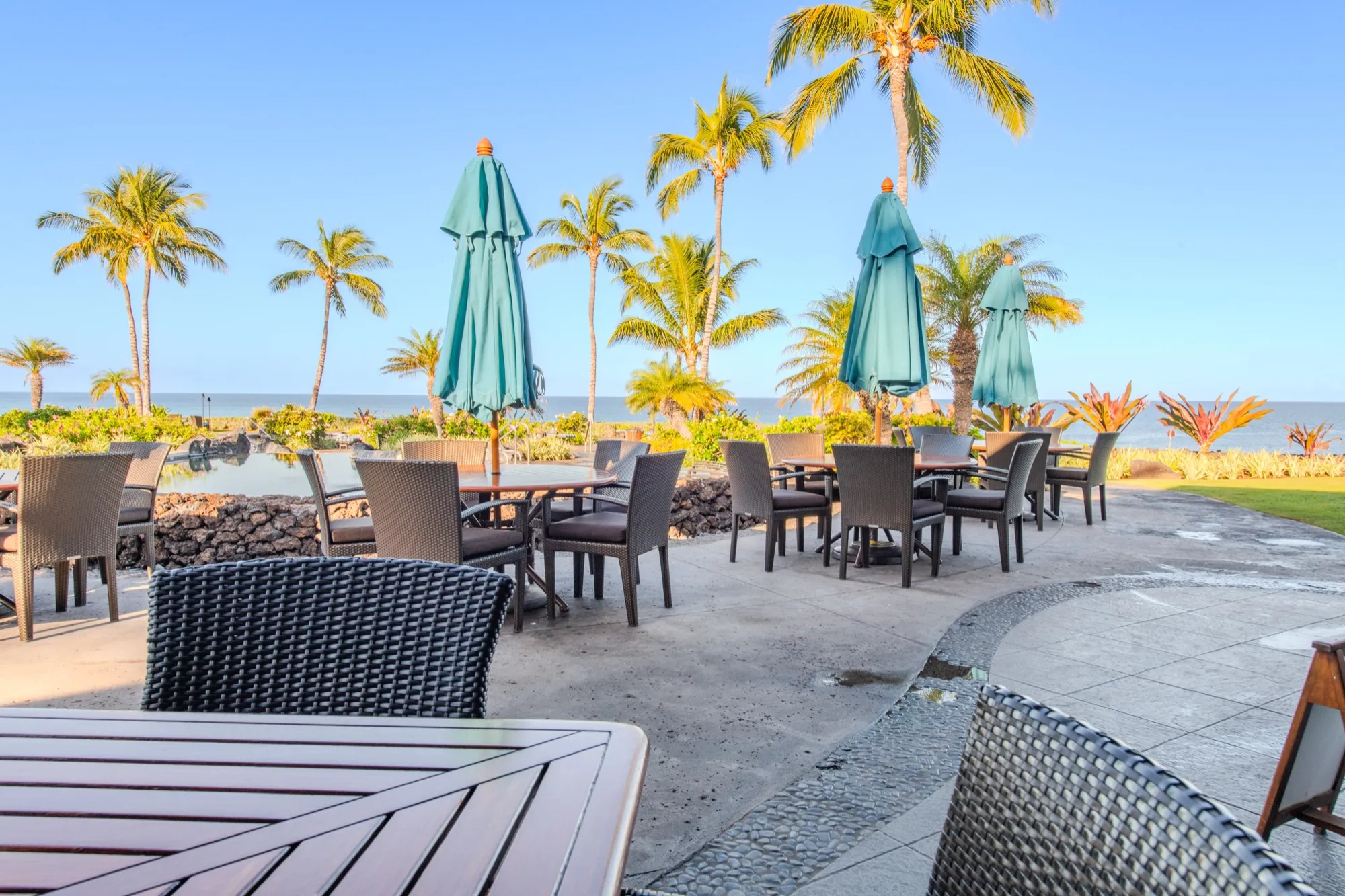 Oceanfront patio dining at the Hali'i Kai Ocean Club restaurant, with palms and umbrellas over the water