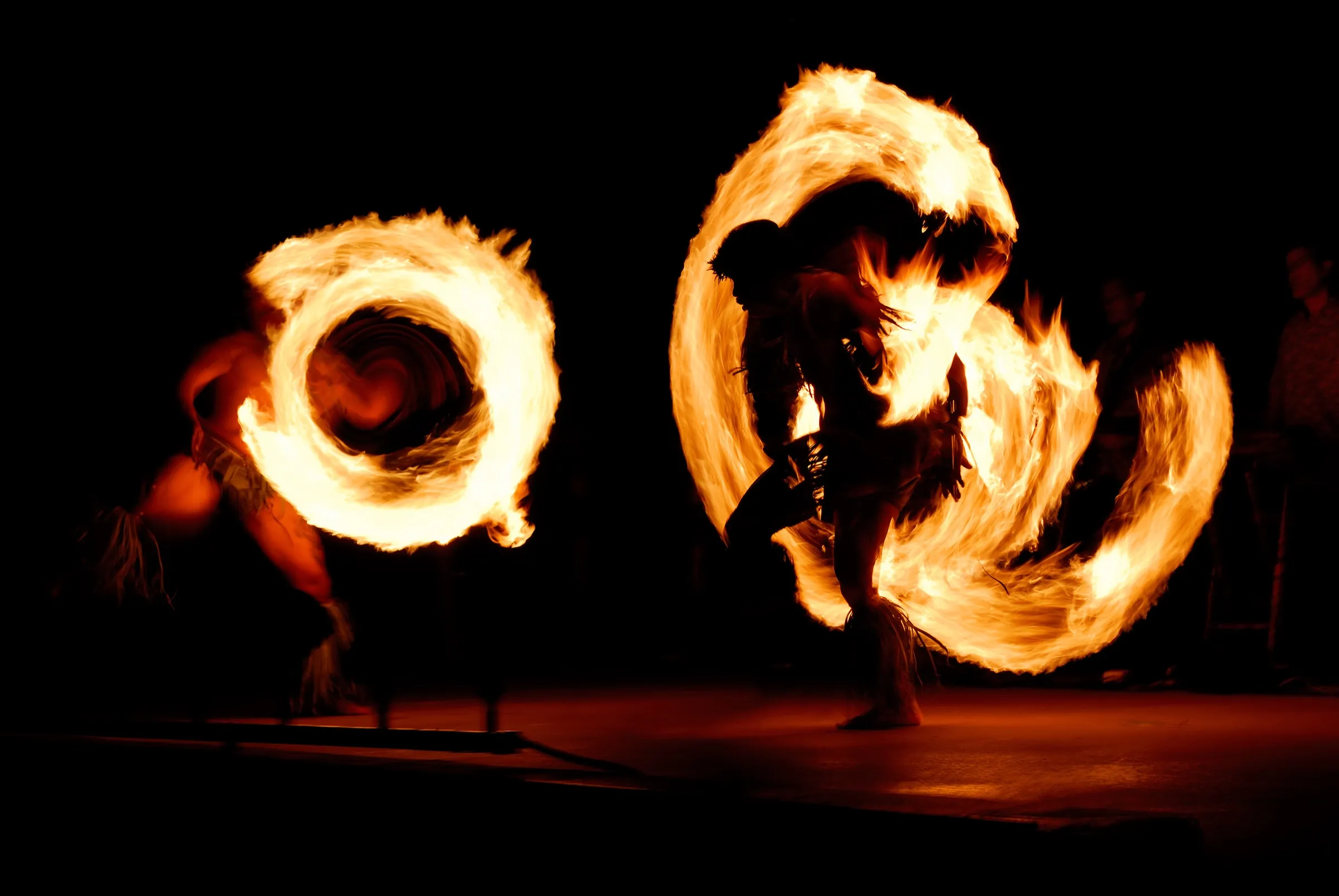 A fire knife dancer performing at an oceanfront luau at sunset