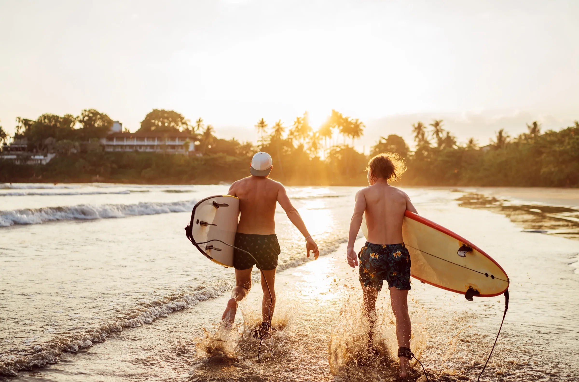 Surfers walking a golden Kona beach carrying their boards at sunset